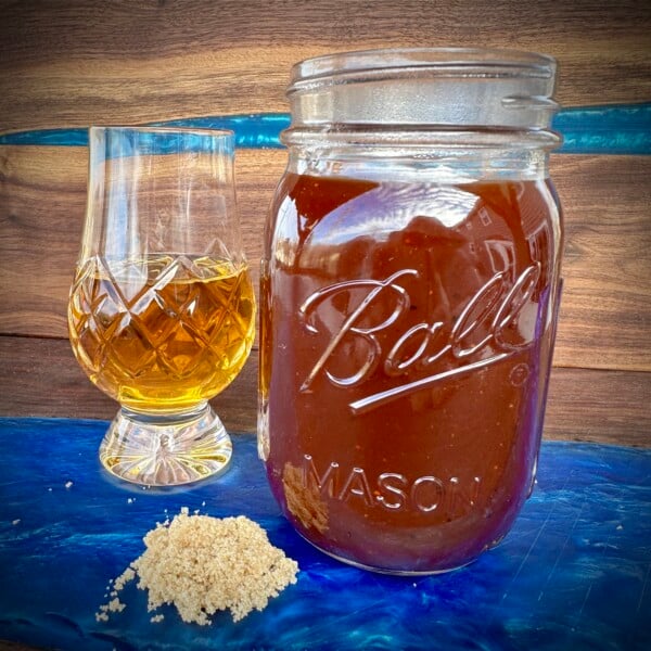 bourbon bbq sauce in a mason jar with a glass of bourbon and a pile of brown sugar.