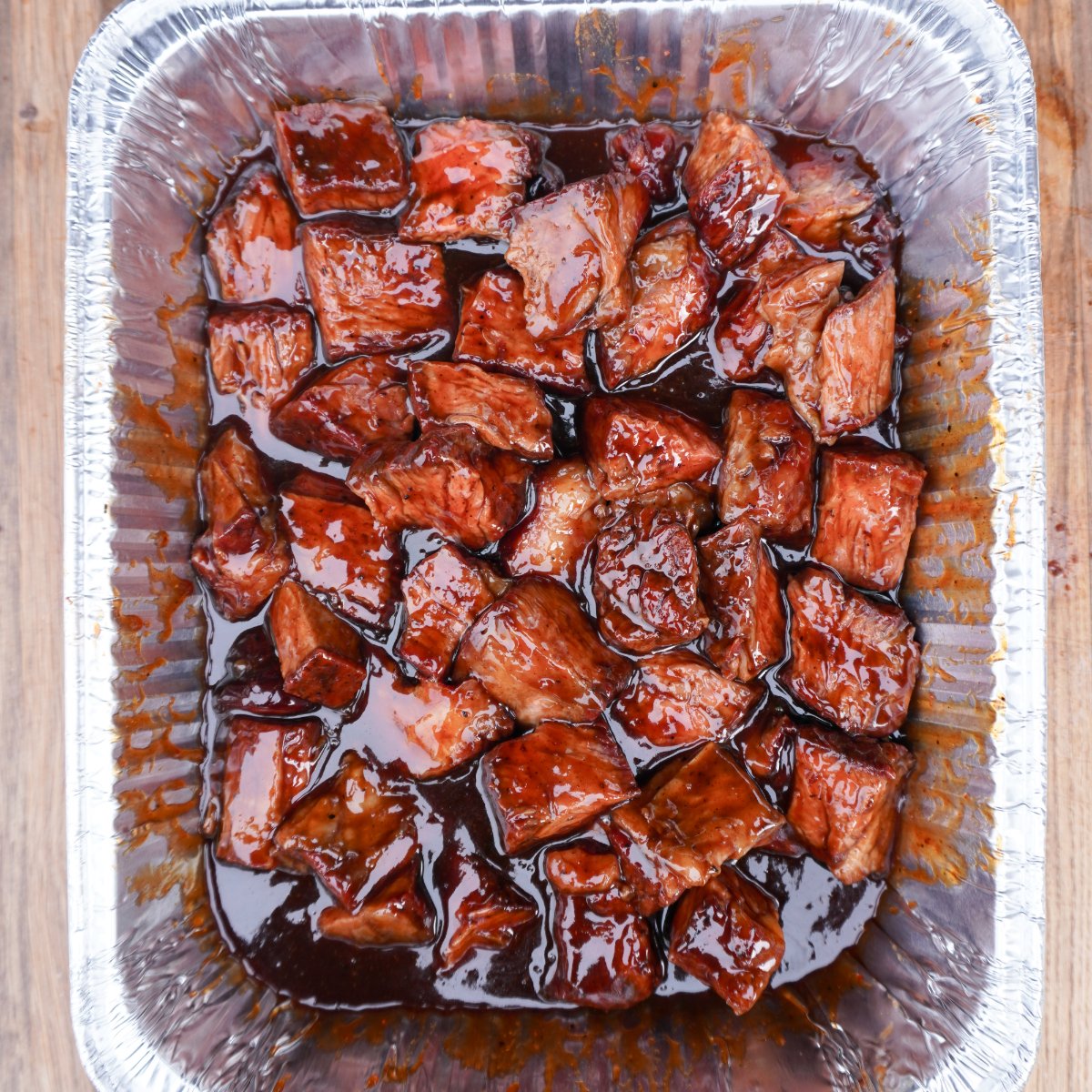 sweet and spicy burnt ends sauced up in a rectangular foil pan.