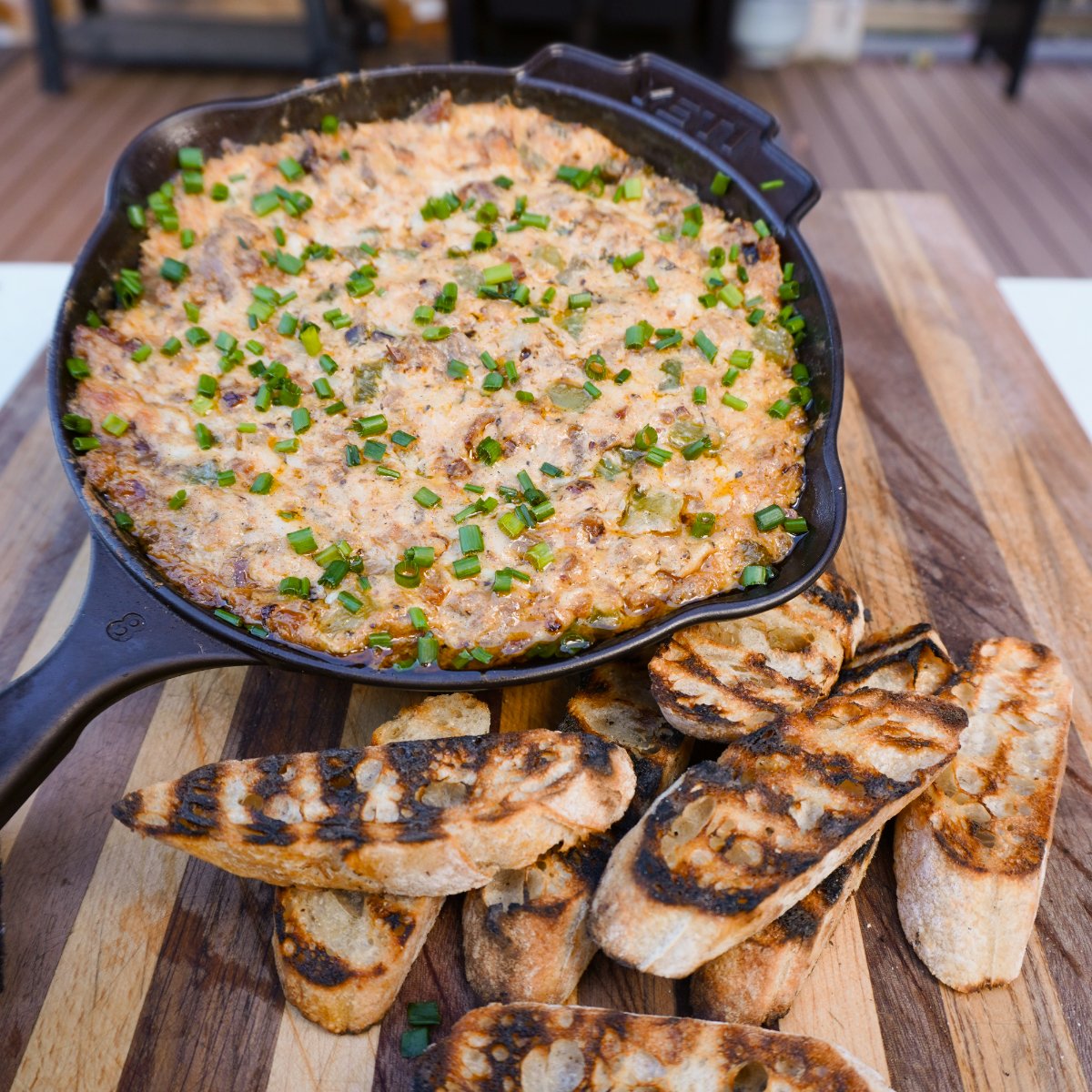 Smoked Cheesesteak dip in a cast iron skillet with a side of toasted bread all on a wooden cutting board.