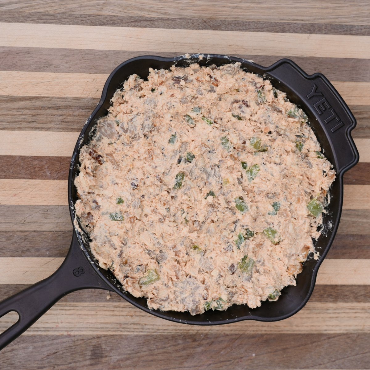 cast iron filled with the cheesesteak mixture on a wooden cutting board.