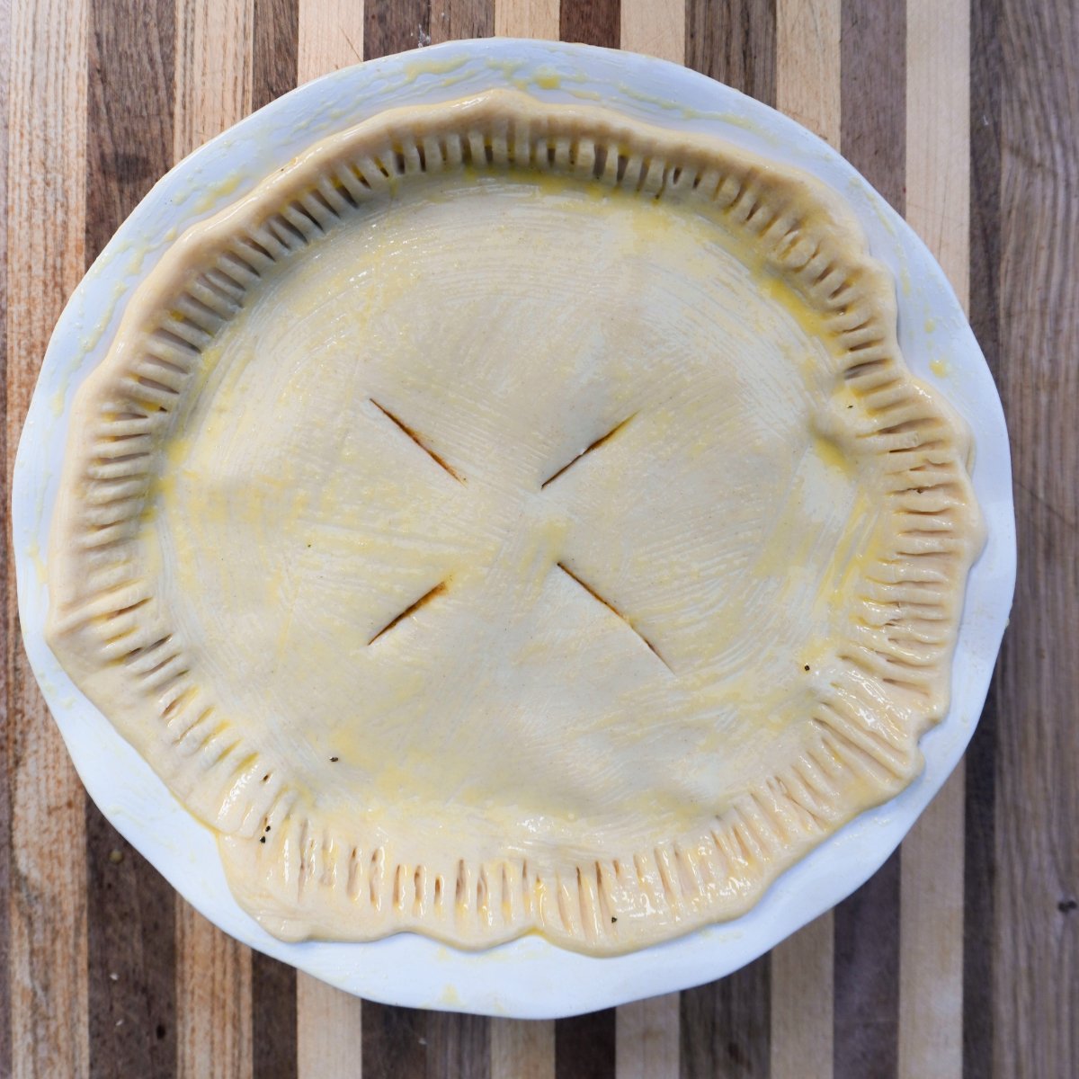 top pie crust with slits and brushed with egg wash in a pie dish ready to be grilled.