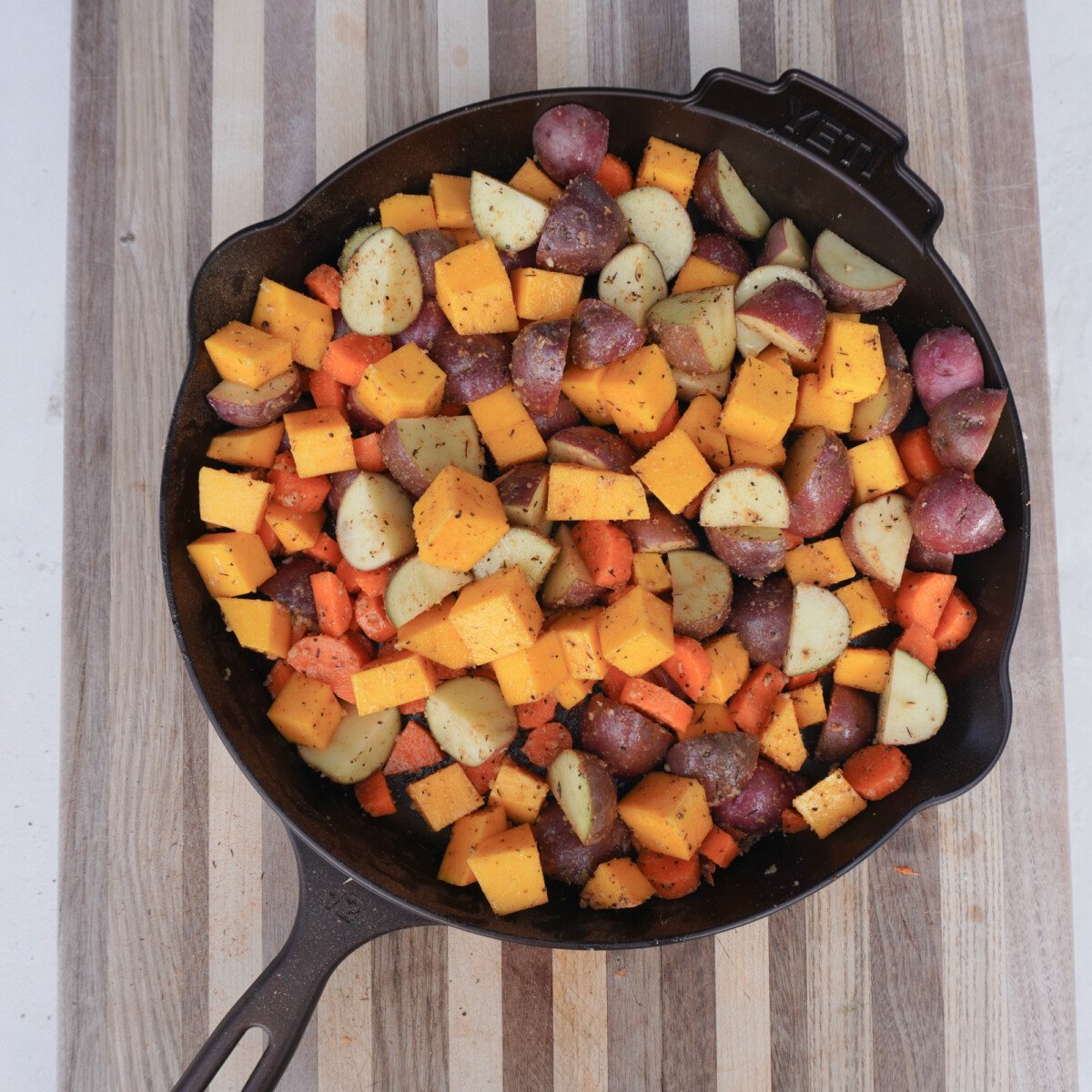 cubed and seasoned veggies in a cast iron skillet.