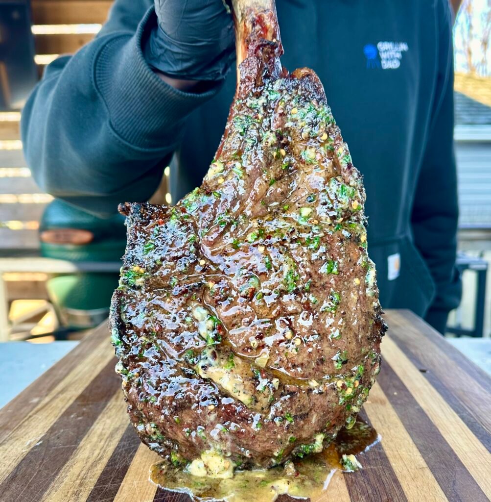 grilled tomahawk steak standing up covered in butter.