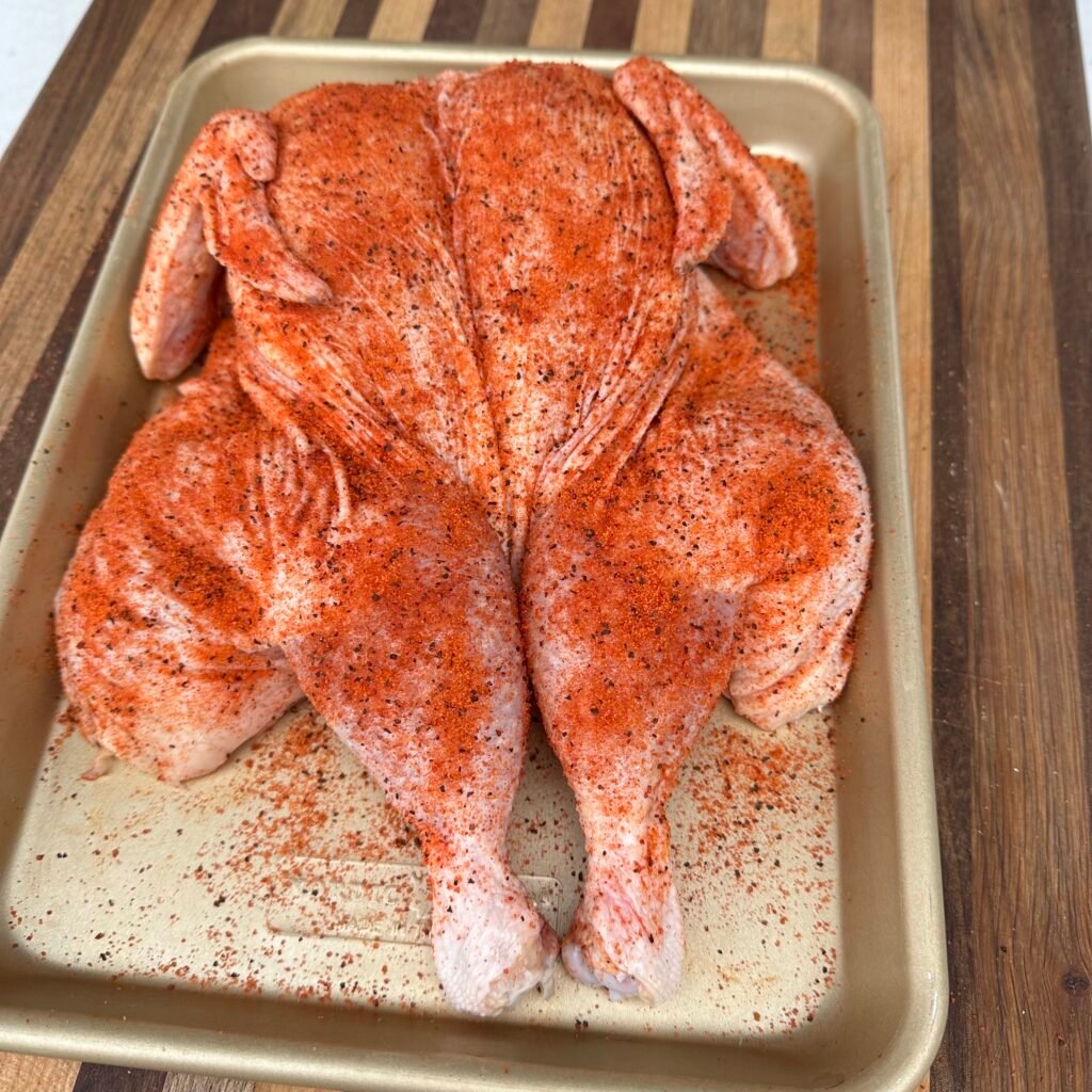 spatchcocked and seasoned chicken on a tray. 