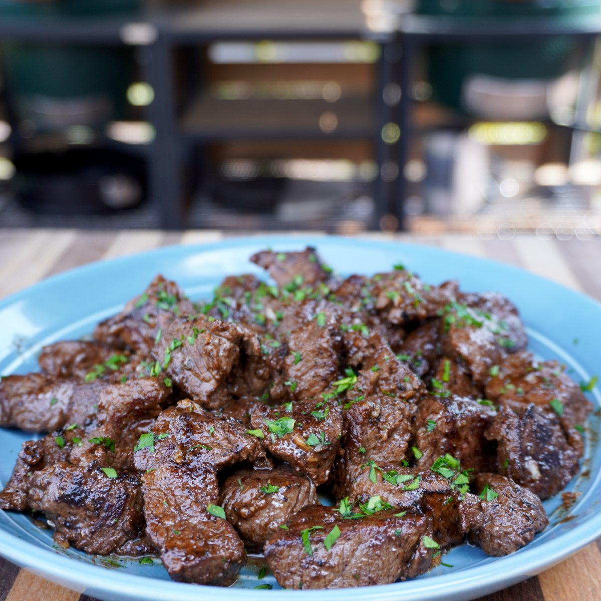 a pile of grilled steak bite plated on a blue plate with chopped parsley sprinkled on top.